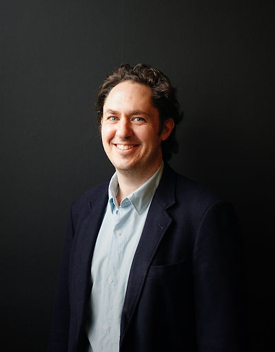 Matthew Andress - Co-founder - Young male in dark blue jacket posing in front of a black wall.