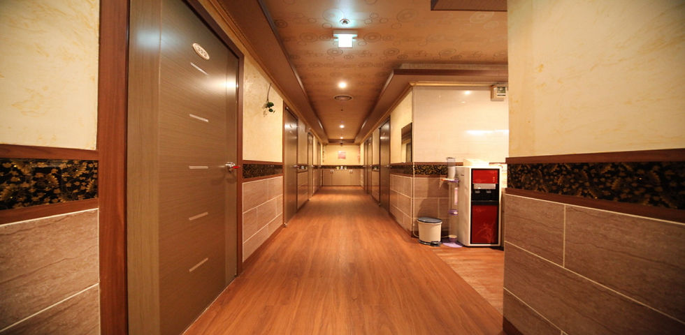 Empty warm-lit hotel corridor with wood floors, lined doors, and a water dispenser on the right.