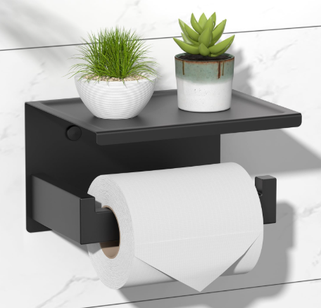 Black wall shelf with a toilet paper roll and two potted plants against a white tiled bathroom wall.