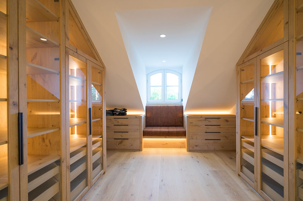 Maßgefertigtes Ankleidezimmer mit beleuchteten Holzschränken und integrierter Sitzbank unter Dachschräge, Innenausbau von Biermann aus Schmallenberg im Sauerland.