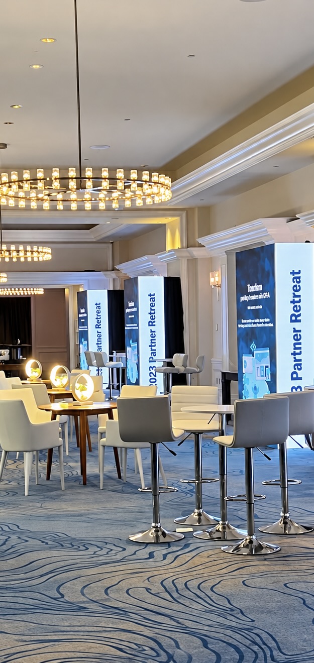 Partner retreat lounge with LED column displays, high-top seating and chandeliers in a hotel ballroom