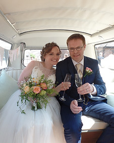 Bride and groom say cheers with champagne glasses in vintage VW campervan