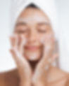 A relaxed woman with a towel wrapped around her head gently massages foaming cleanser into