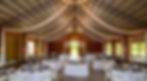 Rustic barn wedding venue transformed with elegant white ceiling drapes, string lights, and round white-clothed tables for a sophisticated farmhouse aesthetic.