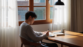 The Power of Self-Reflection — person writing in a journal at a sunlit table beside an open book and a coffee mug by a window.