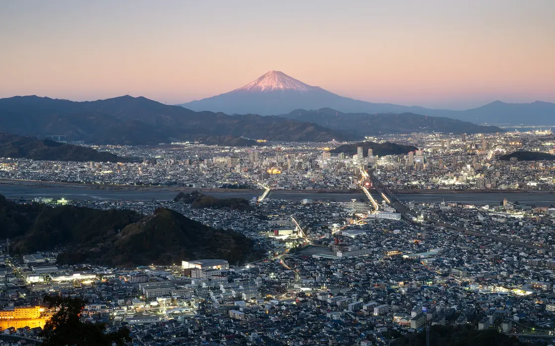 Mount Fuji at dusk viewed from Shizuoka hills with illuminated cityscape – photo by Nicolas Wauters
