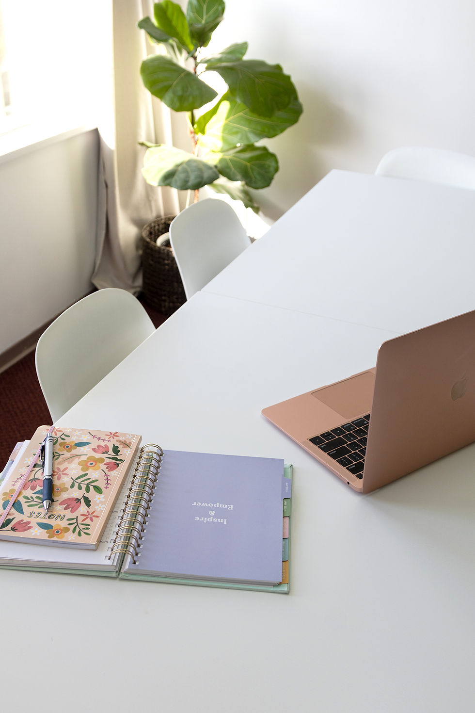 Day planner and notebook beside an open laptop sitting on a white table