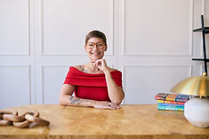 Smiling woman with glasses and red top at desk with books.