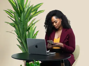 brand strategist typing on a phone while seated in front of a laptop