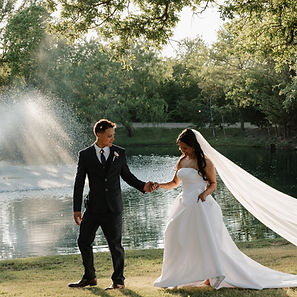 Bride and groom walking hand-in-hand past a scenic lakeside fountain during a DFW wedding venue portrait session, planned by Lasting Events and captured by Anya Joy Photography.