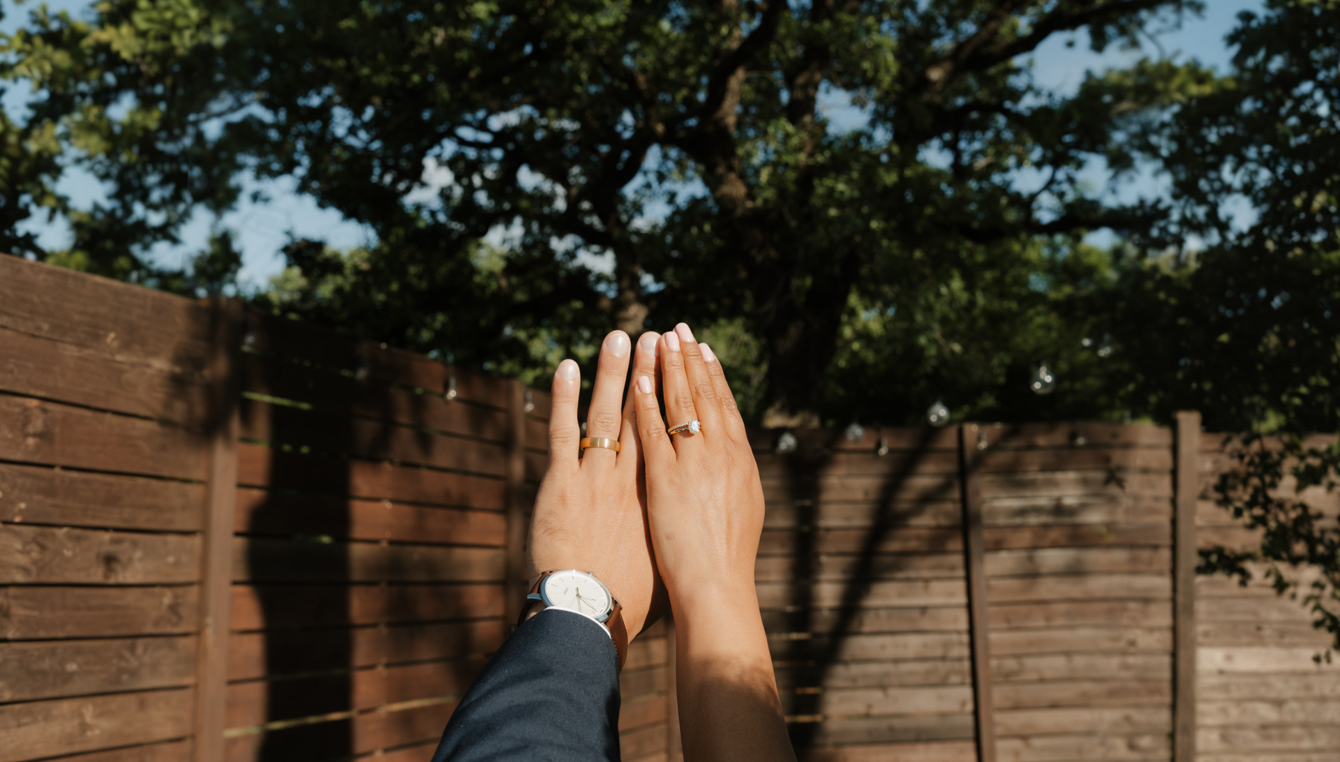 Close up of a bride and groom showing their wedding rings outdoors against a rustic wood fence backdrop at Willow Woods Barn and Studio, planned by Lasting Events DFW.
