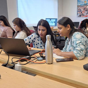 Women collaborating on laptops in an office with a whiteboard and posters.
