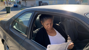Candid photo of a worried person in Modesto looking at bills beside an older car.
