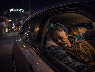 A man sleeps in his car in downtown Modesto, highlighting the challenges of housing insecurity.