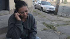A woman, seated on a concrete step with documents beside her, talks on the phone, reaching out to Help Is Hope's Pre-Crisis Program for assistance.