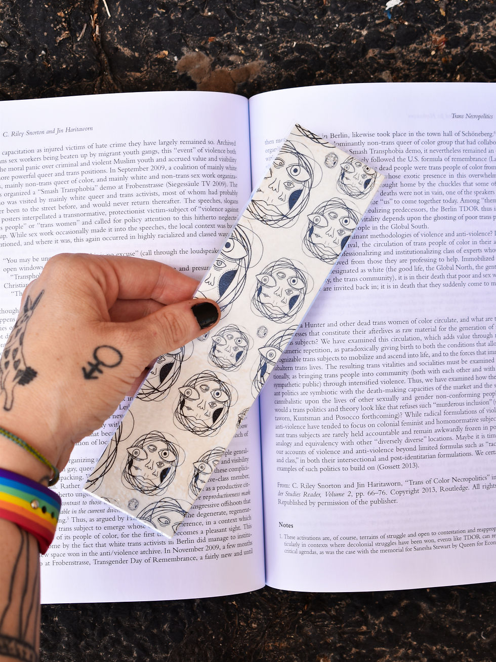 Thumbnail: A long bookmark held over a book. Its pattern consists of chaotic, abstract faces with multiple noses, eyes, and mouths.