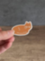 Orange cat sticker being held between fingers.