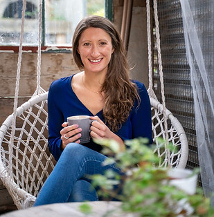 Sophie is looking at the camera and smiling. She's sitting in a hanging chair and holding a grey mug.