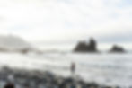 Woman carrying child walks rocky beach