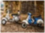 Two vintage scooters parked by brick wall