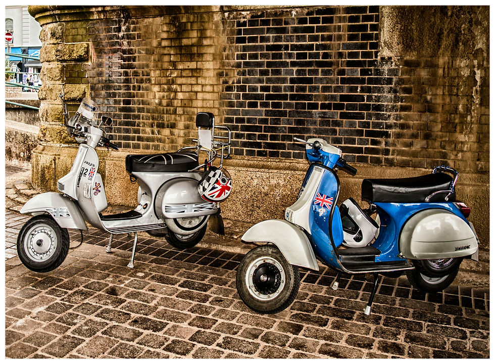 Two vintage scooters parked by brick wall