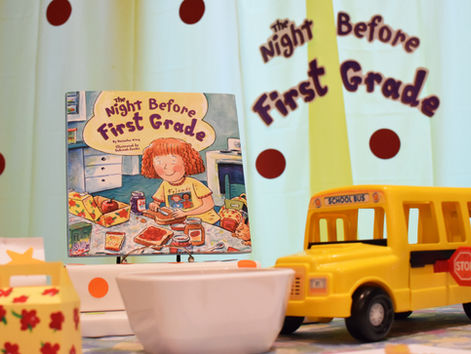 A book called The Night Before First Grade, a toy school bus, a mini lunch box, and a white square bowl