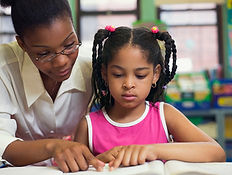 Female teacher with female elementary school child looking at a book