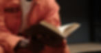African American man in orange prison uniform reads Bible while sitting in cell