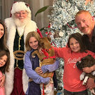 A family stands next to a Christmas tree with Santa Claus. They hold two dogs.