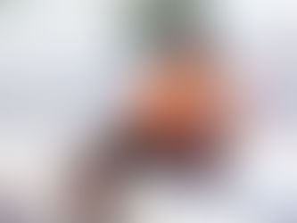 Child in an orange shirt sits on a bench holding a basketball, next to chain-link fence under sunny sky. Text visible on shirt.