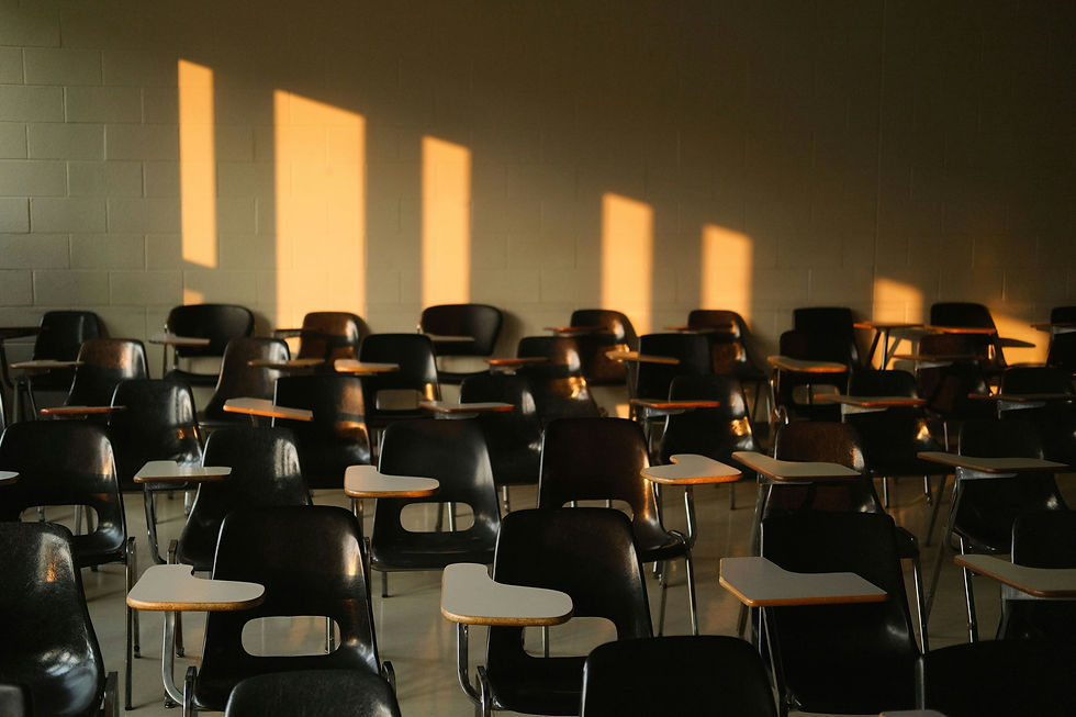 Empty classroom with rows of black desks and chairs, bathed in warm sunlight filtering through windows, creating a serene, quiet ambiance.