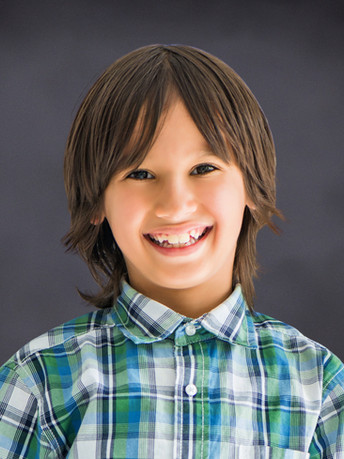 Happy boy with medium-length brown hair and a plaid shirt.