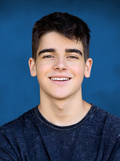 A professional school photo of a smiling teenage boy in a dark shirt, featuring a vibrant blue Horizon background.