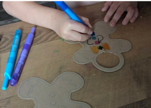 Close-up of young children's hands coloring cardboard gingerbread shapes with markers for a holiday craft.