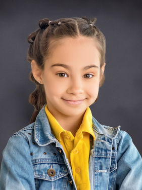 School ID photo of a young girl in a denim jacket on a classic gray studio background