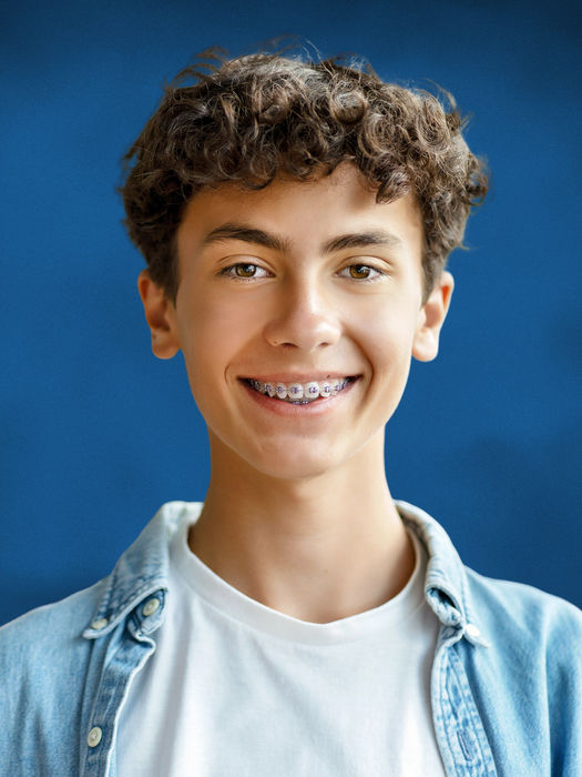 At-home school photo of a teenage boy with curly hair and braces on a classic blue school photo background
