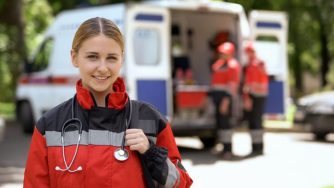 Female paramedic smiling into camera, ambulance crew blurred on background.jpg