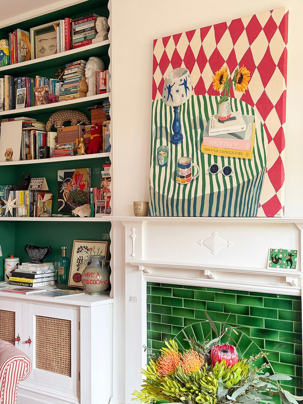 Colourful room with a patterned painting above a white fireplace. Green tiled hearth, vibrant bookshelves, and a vase of flowers create a lively mood.