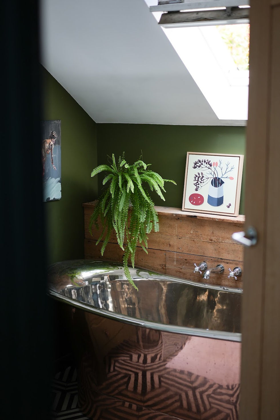 Bathroom with a metallic tub, green walls, and a fern. Wood paneling, framed plant artwork, and geometric floor tiles. Skylight view.