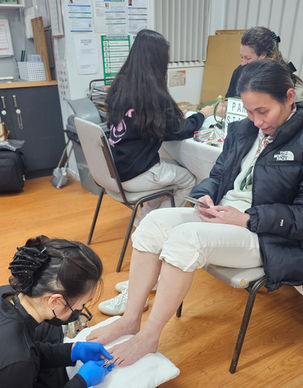 A seated guest receiving mobile nail care, with a beauty professional working at her feet.