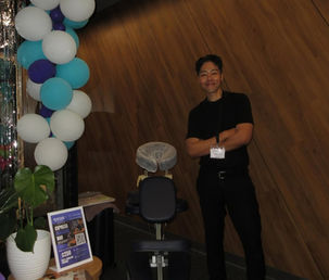 A massage therapist standing beside a portable massage chair and a blue, green and white balloon display.