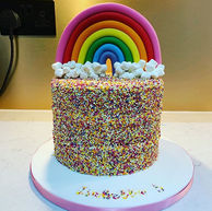 Three layers of sponge with a buttercream filling coated in sprinkles and topped with a sugarpaste rainbow with mini marshmallow clouds