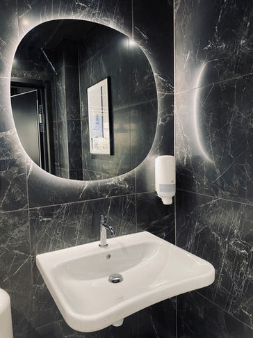 Mörk badrum med 60x60 plattor och rund spegel med handfat