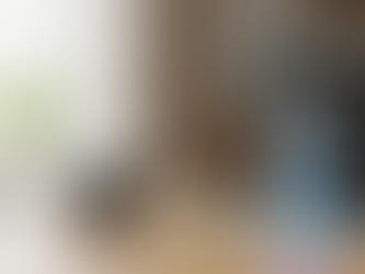 Smart speaker on a laptop glows blue, indicating activity. A small round device displays a lock icon. Bright room with a plant in view.