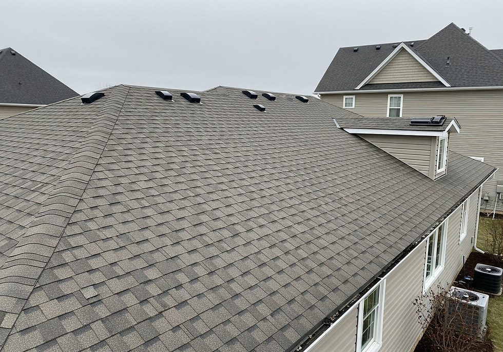 Gray shingled roof with multiple vents, under cloudy sky. Beige house in background, windows and air conditioning units visible.