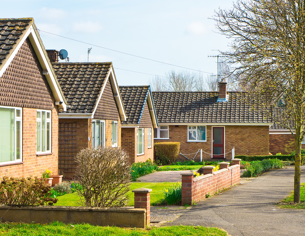 Row of brick houses with dark roofs on a sunny day, framed by leafless trees and green lawns. A peaceful residential setting.