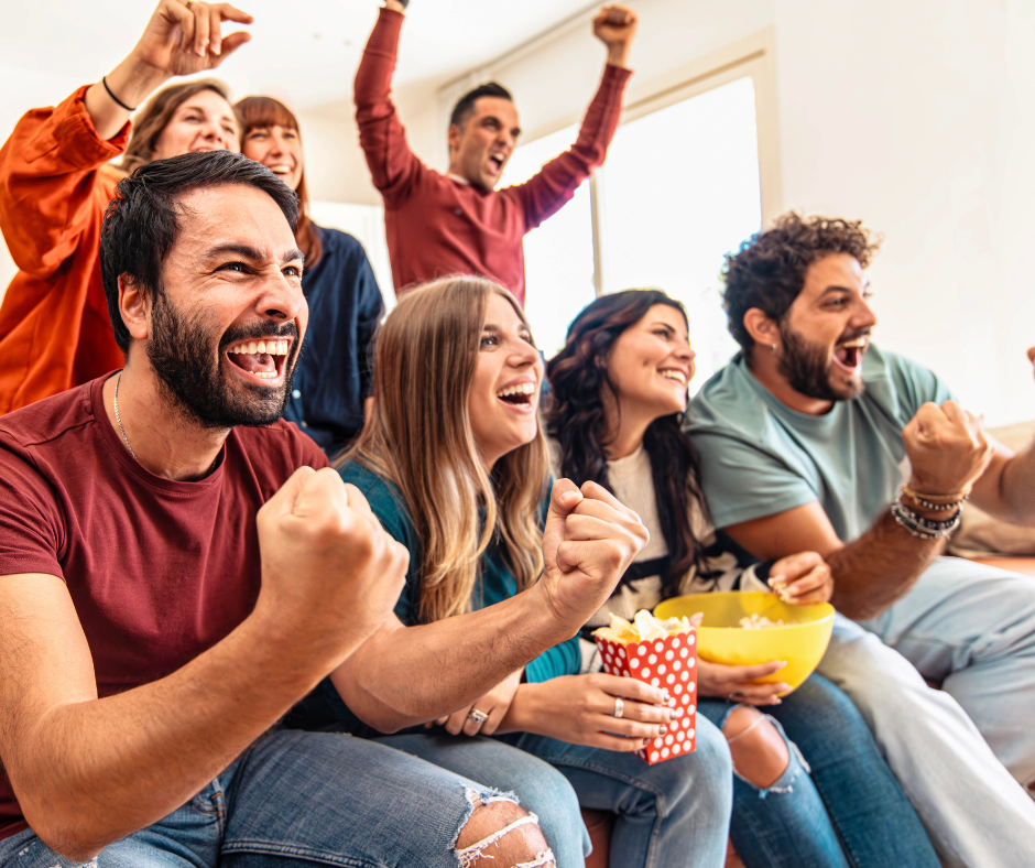 Group of men and women sitting down cheering and eating popcorn