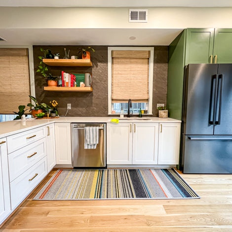 Contemporary kitchen featuring white shaker cabinets, gold handles, floating wood shelves, and a black fridge with a striped rug