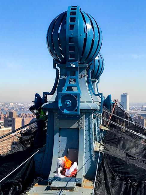 A newly installed decorative globe atop the Manhattan Bridge, restored to its original grandeur, overlooking the New York City skyline.