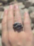 Hand wearing handmade silver organic texture ring on pebble background